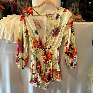 Ivory long sleeve romper with colorful floral and pompom details, zipper back